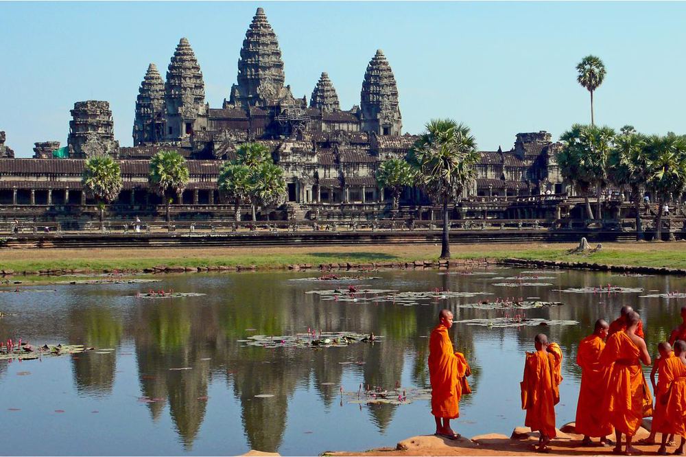 Mnisi w pomarańczowych szatach nad stawem przed świątynią Angkor Wat w Kambodży